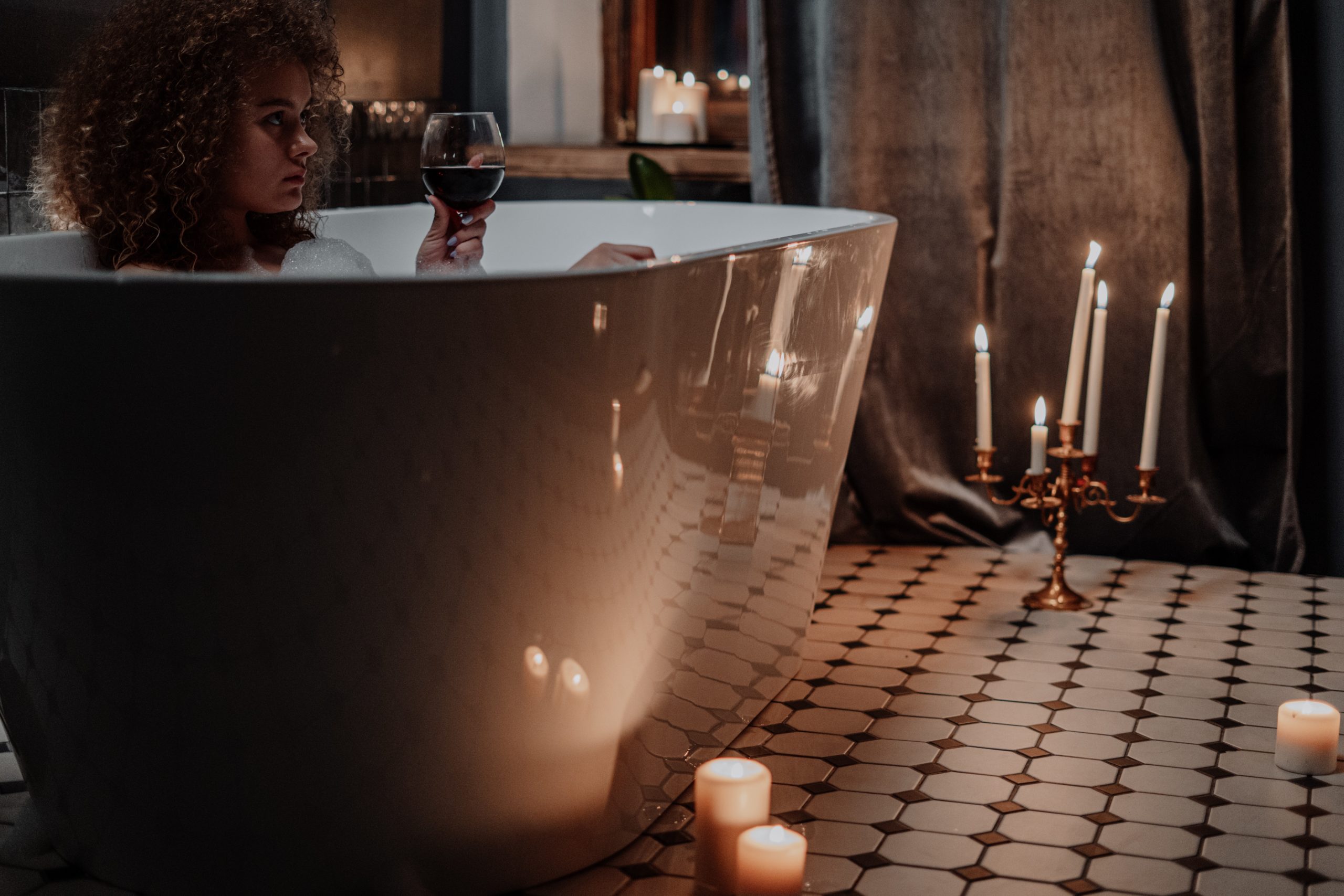 Woman in a luxury bath, drinking from a wine glass and surrounded by candles